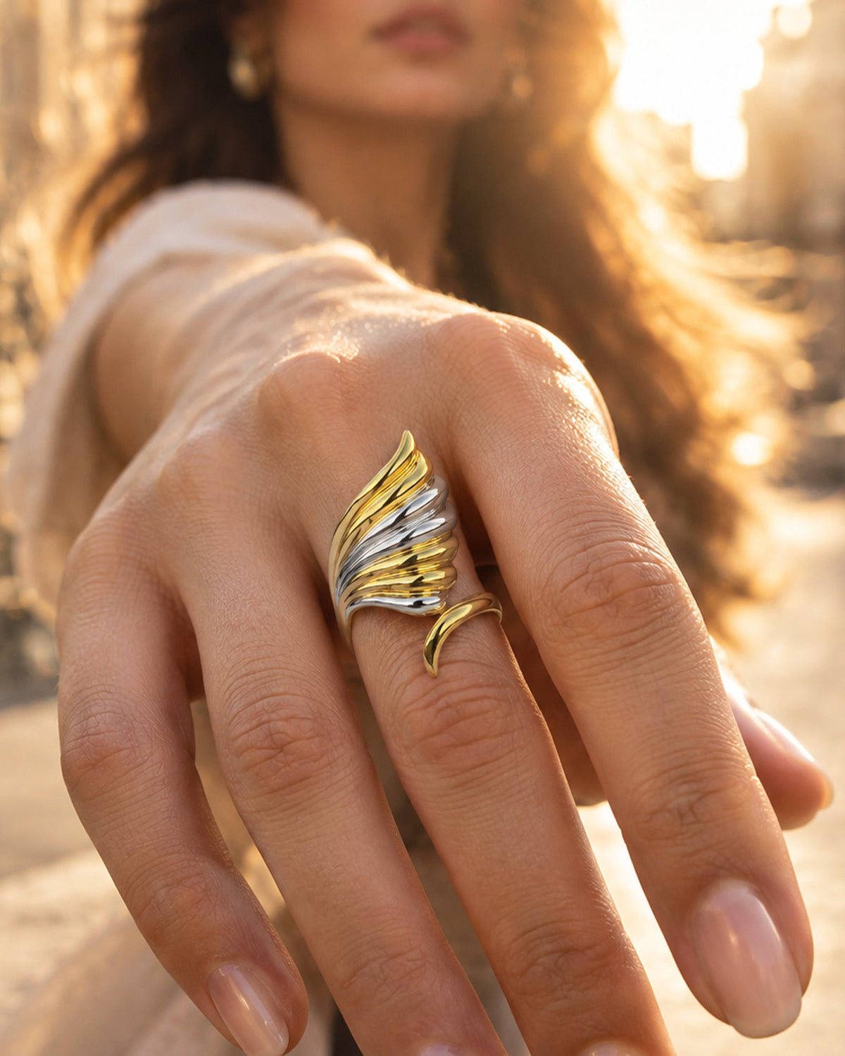 Close-up of woman's hand wearing two-tone silver & gold wave ring, outdoors in soft golden natural sunligh