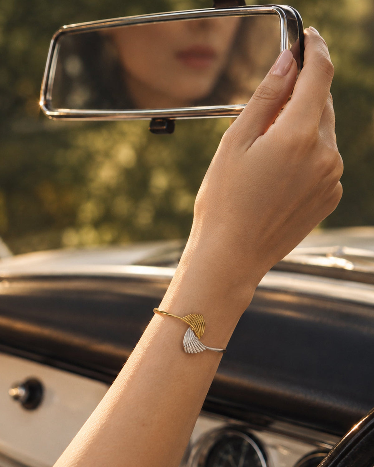 Model wearing dual-tone gold & silver wave cuff bracelet adjusting vintage car mirror, lifestyle Brand image.