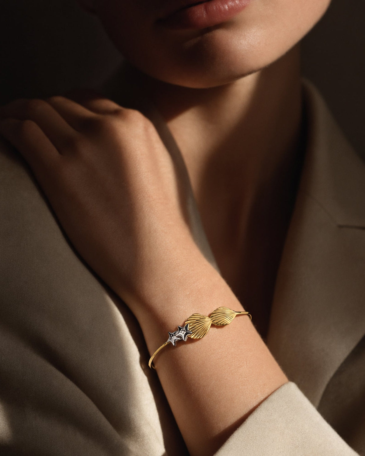 Model wrist wearing gold vermeil seashell cuff bangle for size guide, styled with neutral blazer in soft lighting.