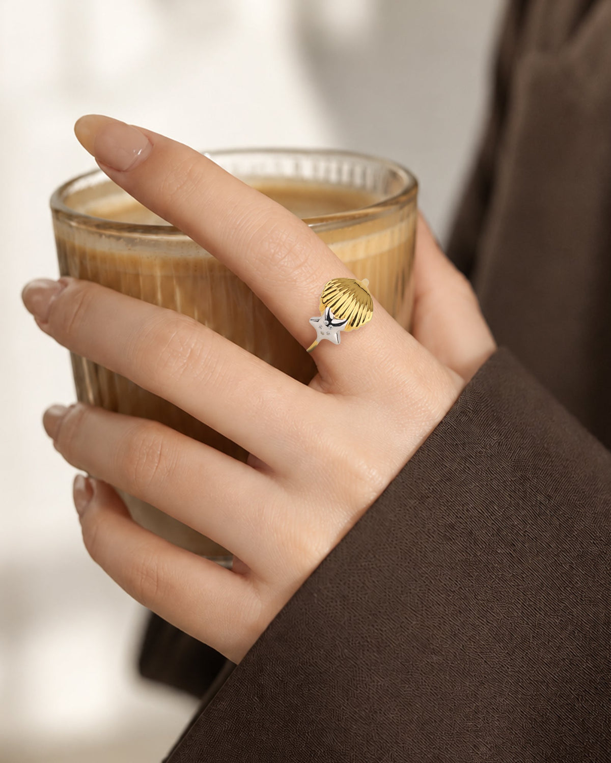 Model wearing dual-tone seashell starfish ring holding coffee cup; ring size guide, styled in dark brown blazer.