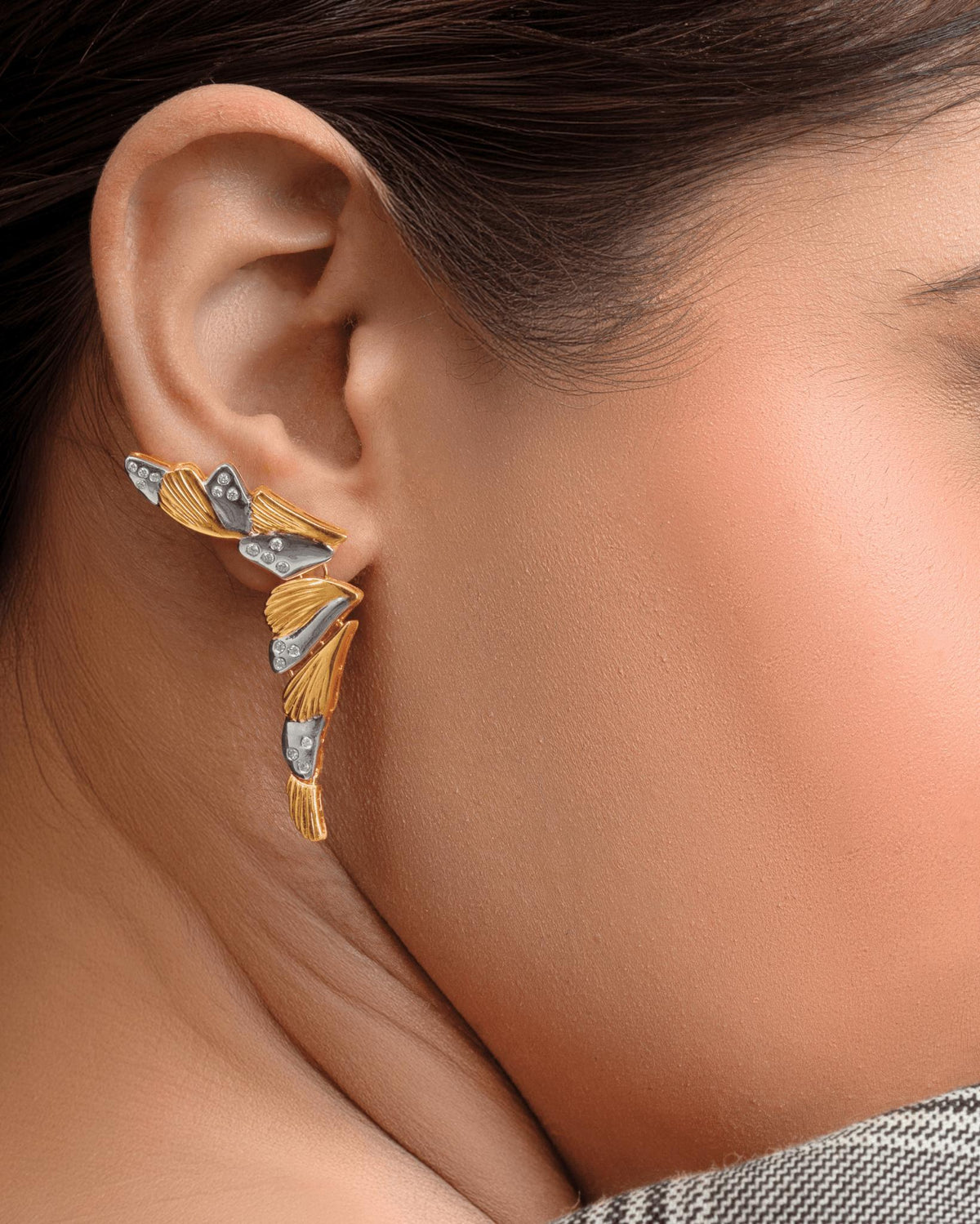 A close-up of a woman's ear wearing a unique, multi-piece gold and silver earcuff with leaf-like details.