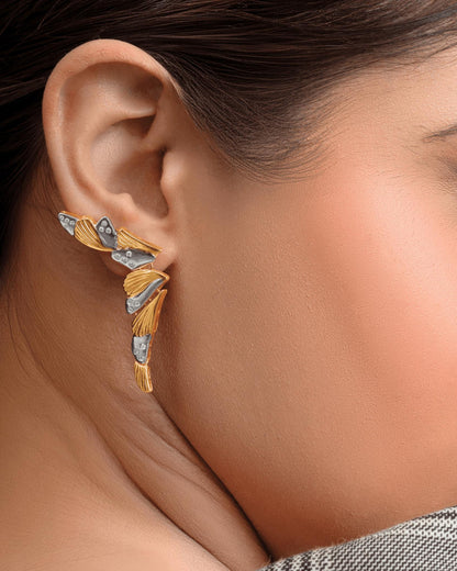 A close-up of a woman's ear wearing a unique, multi-piece gold and silver earcuff with leaf-like details.